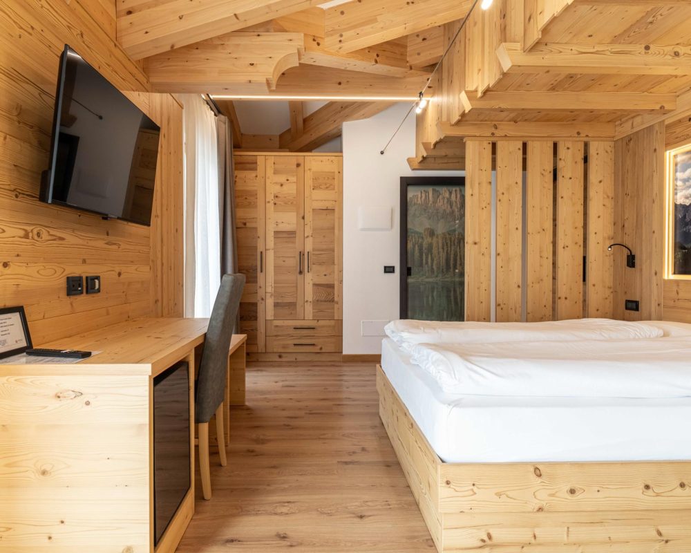Vista frontale del letto matrimoniale nello Chalet Alaska con il murale retroilluminato di montagne, armadio in legno su misura e dettaglio del divano letto verde Oliva.
