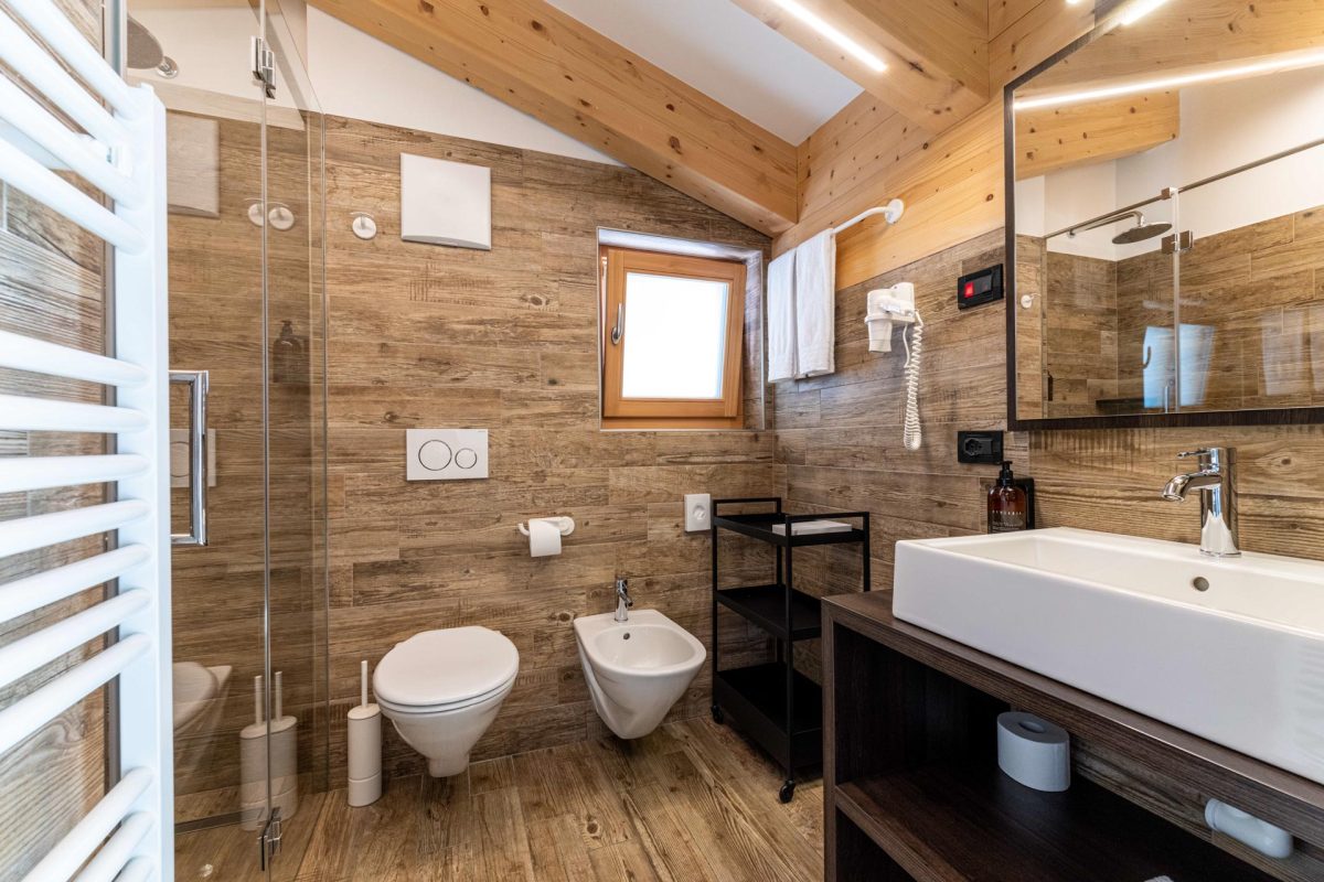Bagno moderno rivestito in gres effetto legno con box doccia in cristallo, lavabo di design e sanitari sospesi.